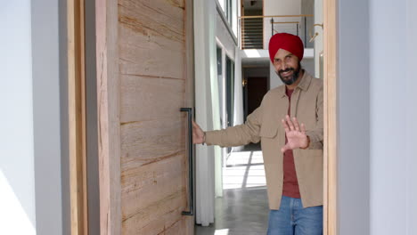 welcoming guests, man in turban smiling and opening front door of home