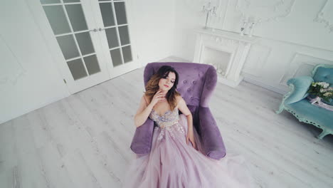 luxury young woman with perfect makeup and beautiful dress in a chair in studio. attractive bride in wedding dress is posing to camera while sitting in armchair in stylish room.