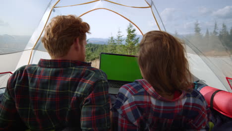 Focused-man-and-woman-watching-movie-on-laptop-with-green-screen-in-tent