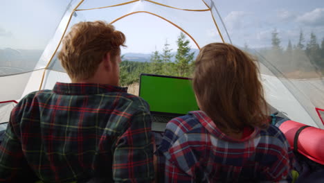 focused man and woman watching movie on laptop with green screen in tent