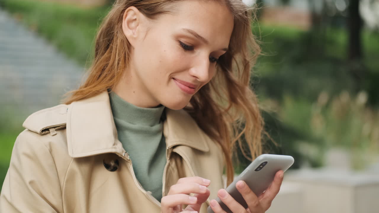 Happy Caucasian female student using smartphone outdoors.