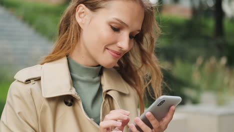 feliz estudiante caucásica usando el teléfono inteligente al aire libre.