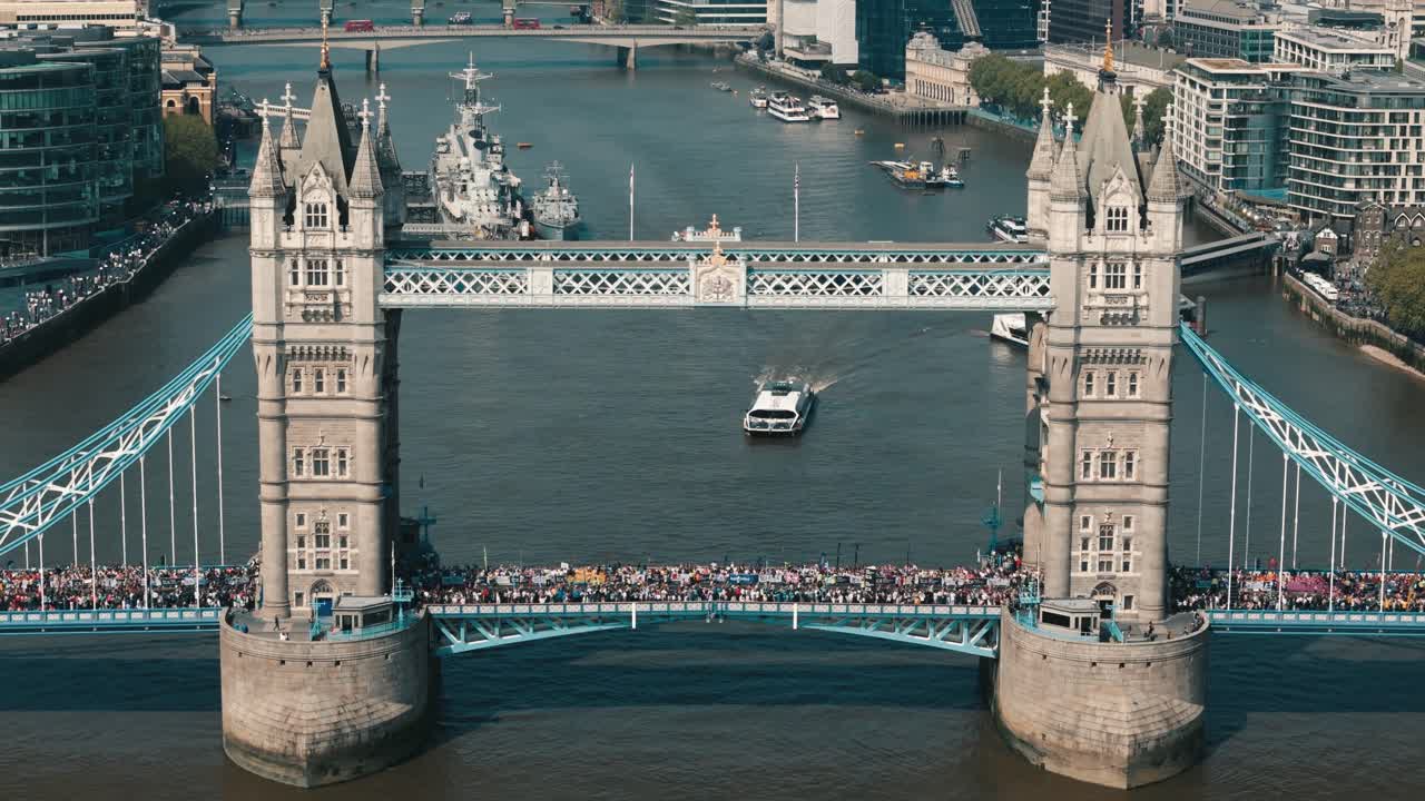 Wide static view of Tower Bridge with marathon runners and a boat passing beneath on a sunny London day