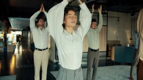 a blonde business girl in a white shirt is doing yoga with her colleagues in the office. take a break from work to maintain spiritual strength and stability