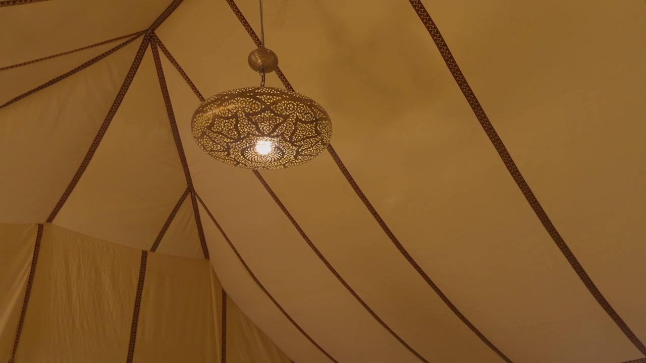 Decorative brass lantern glowing inside a draped fabric tent ceiling at a Moroccan desert camp
