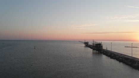 Aerial-panoramic-view-of-a-trabucco-silhouette,-a-traditional-fishing-machine,-on-the-italian-coastline,-at-sunset