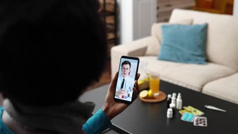 sobre el hombro de una mujer afroamericana que tiene una consulta médica en línea con un médico caucásico en un teléfono inteligente