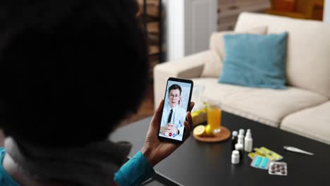 over shoulder of african american woman having online medical consultation with caucasian male doctor on smartphone