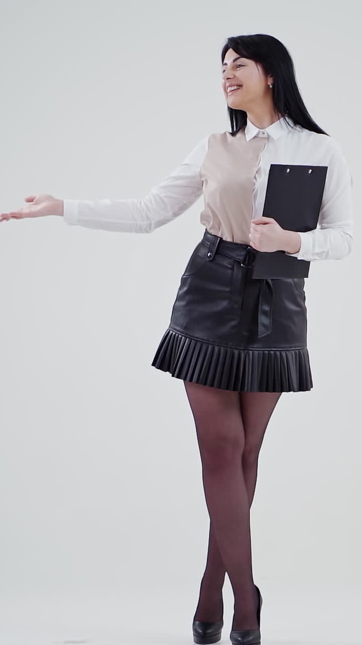 Charming young business woman in studio. Full-length portrait of smiling female in short skirt isolated on grey background holds folder. People sincere emotions. Vertical video