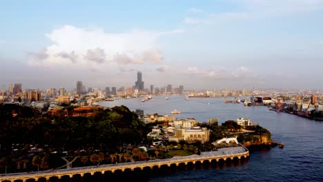 A-coastal-city-skyline-at-sunset,-with-calm-waters-and-scattered-clouds,-aerial-view