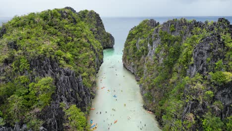 dolly aérea entre los acantilados rocosos de el nido mientras los turistas nadan en el agua de palawan