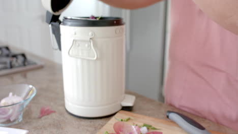 Midsection-of-plus-size-biracial-woman-composting-vegetable-waste-in-kitchen,-slow-motion