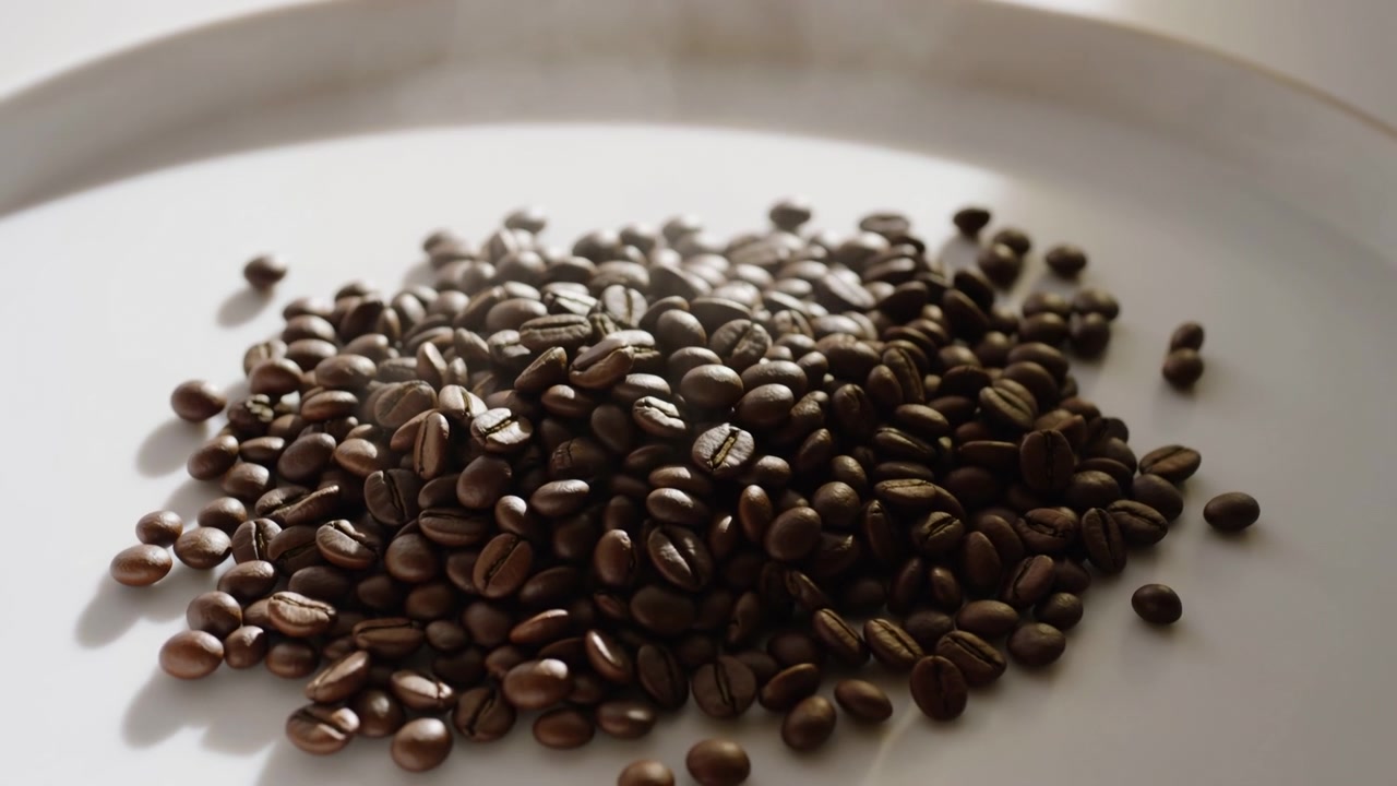 Primo piano dal basso di chicchi di caffè tostati medio-scuri che riposano in un piccolo mucchio su un piatto bianco piatto, con dettagli nitidi in primo piano, texture lucide, ombre morbide e una calda luce da studio neutra.