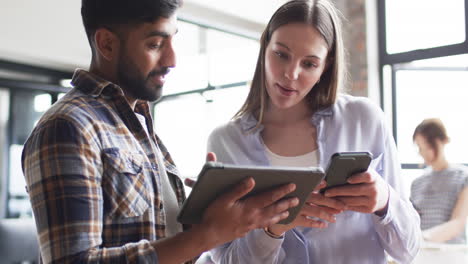 joven mujer caucásica y hombre asiático revisan el contenido del negocio en una tableta juntos