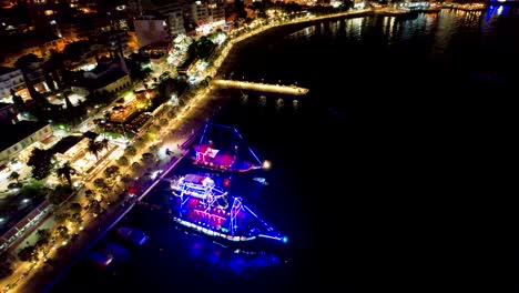 Sarandas-Sommerliche-Ruhe-Bei-Nacht,-Menschen-Flanieren-Auf-Der-Promenade-Und-Genießen-Einen-Urlaubsabend-Am-Hafen-Mit-Beleuchteten-Ausflugsschiffen