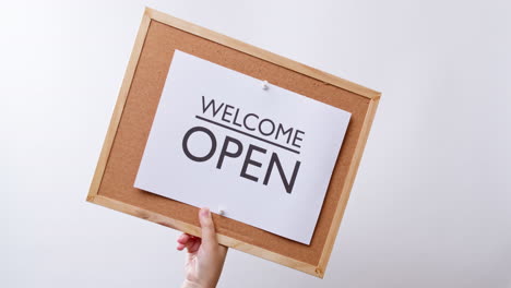 Woman's-hand-shows-the-paper-on-board-with-the-word-Sorry-CLOSED-and-flips-it-to-Welcome-OPEN-in-white-studio-background-with-copy-space