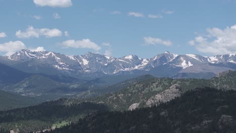 Serene-Landscape-of-Rocky-Mountains-on-Hot-Summer-Day,-Drone-Shot-of-Snow-Capped-Peak-Above-Green-Valley