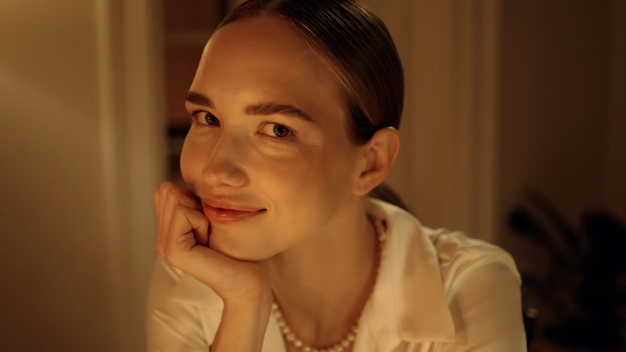 매혹적인 여자가 저녁에 집에서 카메라를 쳐다보고 있다. 여자애가 포즈를 취하고 있다.