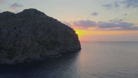 sideways revealing drone shot of the sunset at sa calobra, mallorca, spain behind a big mountain above the mediterranean sea