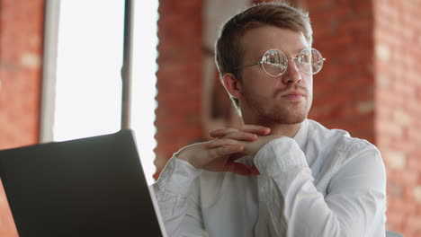 portrait of handsome european man with glasses and laptop in cafe freelancer is sitting alone and thinking