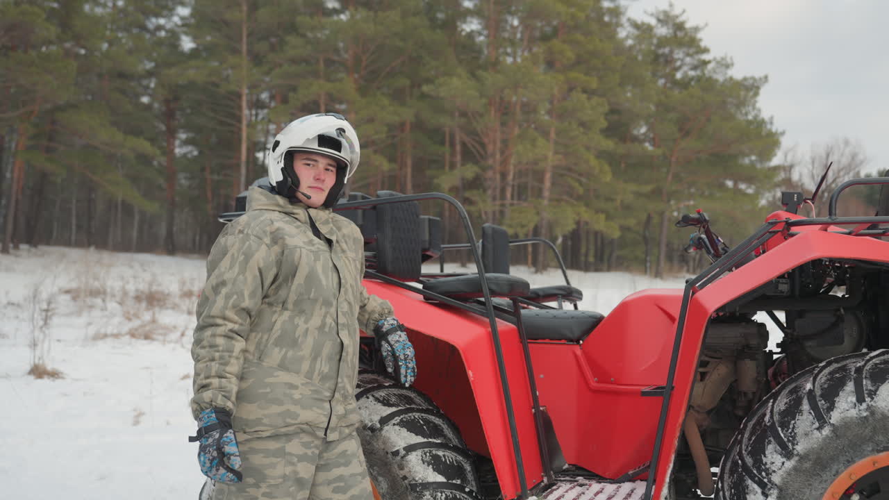Equipaggio caucasico attorno a un ATV rosso che si scambiano i caschi e si preparano a salire in una radura di pini innevata, giacche e guanti mimetici, assistenza pratica e cameratismo di gruppo, momento di lancio dinamico.