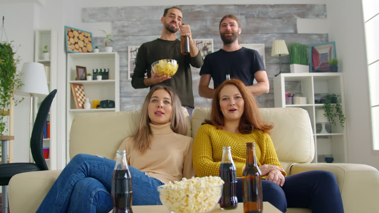 Junge Frauen sitzen lächelnd auf dem Sofa und sehen fern