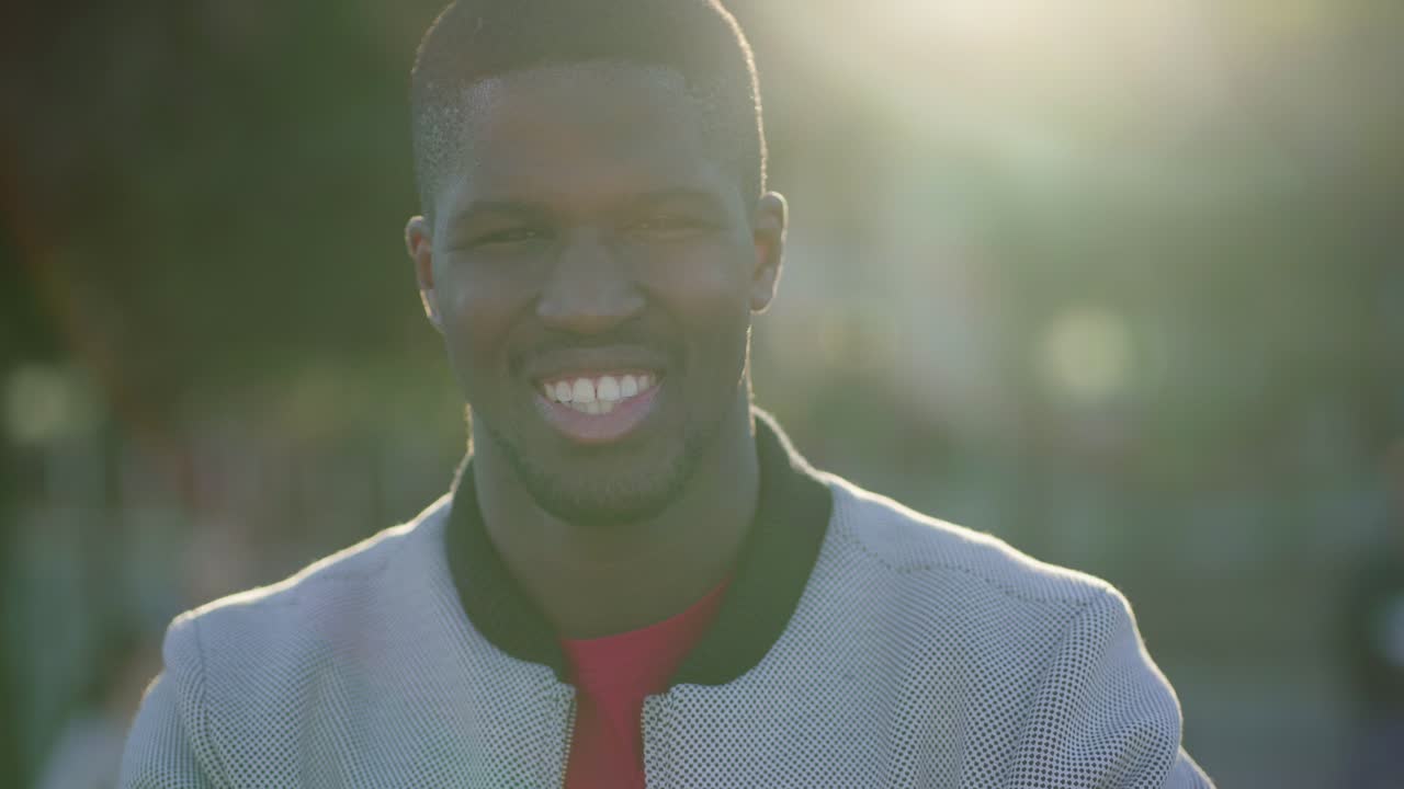 Young man standing in park, looking at camera, smiling