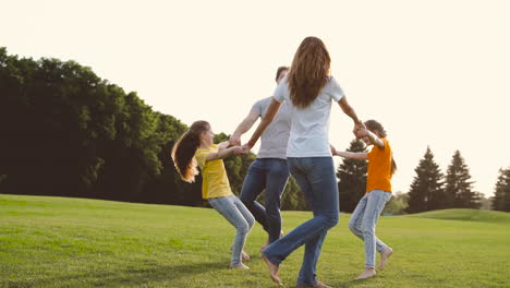 pais felizes e filhas de mãos dadas e girando no campo de grama verde no parque 1