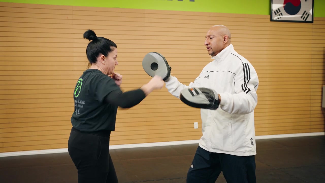 Seorang Wanita Paruh Baya dalam Tangkapan Jarak Menengah Melakukan Latihan Tanding Rentetan Pukulan Kombinasi Teknik Bela Diri dengan Master Sabuk Hitam Taekwondo, Tinju, Karate, Kung Fu di Dalam Studio Gym Latihan Profesional