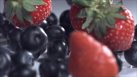 blueberries and strawberries rolling down on white background. slow motion