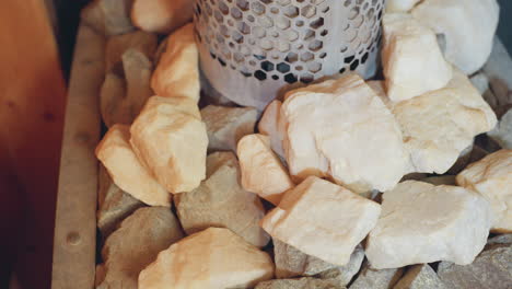 close up of mixed sauna stones, pale and dark, arranged around perforated metal heater in steam room, capturing raw rocky textures, soothing earth tones
