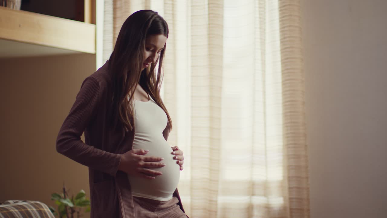 임신 한 여자 가 창문  에서 배 를 만지고 있다