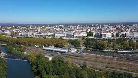 Antena-De-La-Estación-De-Tren-De-Pau-Viajando-Sobre-El-Río-Con-La-Ciudad-Al-Fondo