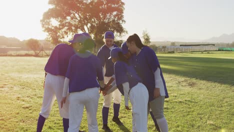 diverse group of female baseball players on sunny pitch, in a huddle, stacking hands