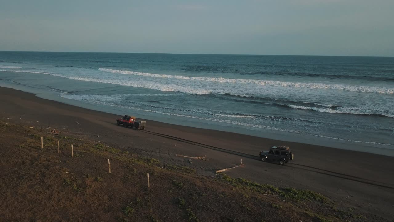 increíble toma aérea de drones de autos 4x4 conduciendo sobre arena negra, olas rompiendo, viaje de campamento en san jose, guatemala