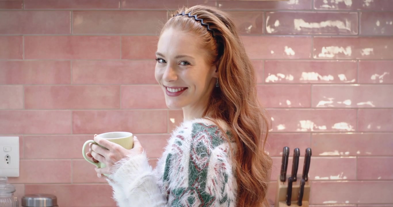 Donna che tiene una tazza verde in cucina, numeri che si materializzano, alzando la tazza, sorseggiando, girandosi, sorridendo