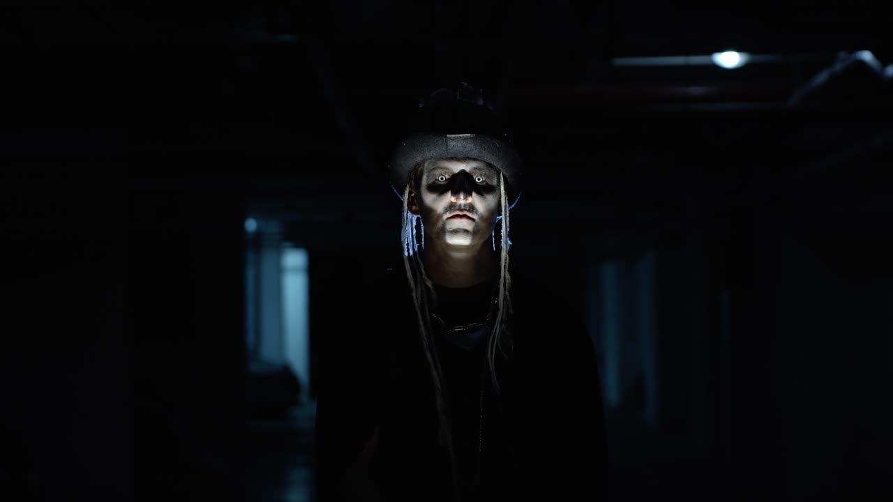 hombre espeluznante con maquillaje de esqueleto que aparece de la oscuridad cuando la luz cae sobre él, haciendo caras