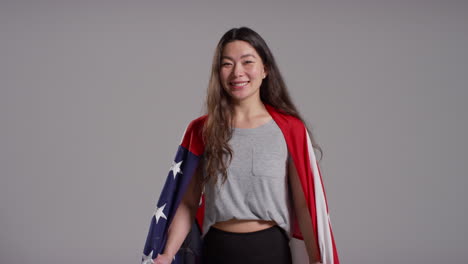 studio portrait shot of woman wrapped in american flag celebrating 4th july independence day 4