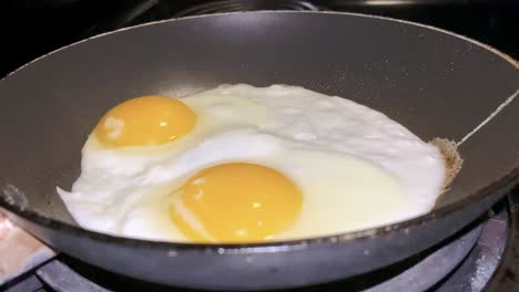 uhd, hfr, close up shot of two sunny side up eggs cooking in an old skillet on an electric stove in the morning for breakfast.