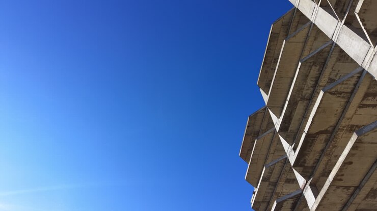 Toma arquitectónica en ángulo bajo de losas de hormigón sobresalientes y esquinas de un proyecto residencial. Esquina de edificio de hormigón sin terminar contra un cielo azul claro. Aéreo.