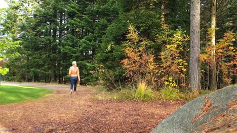 blonde female walking down the trail by evergreen forest with some autumn foliage on sunny day