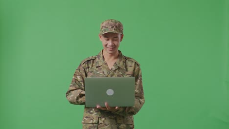 asian man soldier using a laptop while standing in the green screen background studio