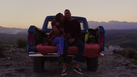 Young-couple-on-a-road-trip-sitting-outside-on-their-truck-at-dusk