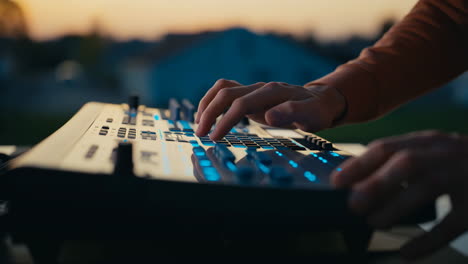 hands playing an electronic music synthesizer at dusk