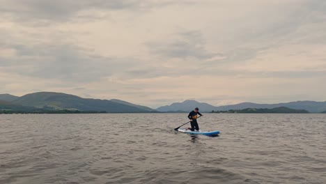 static shot of a young man heading back into shore on his stand up paddle board