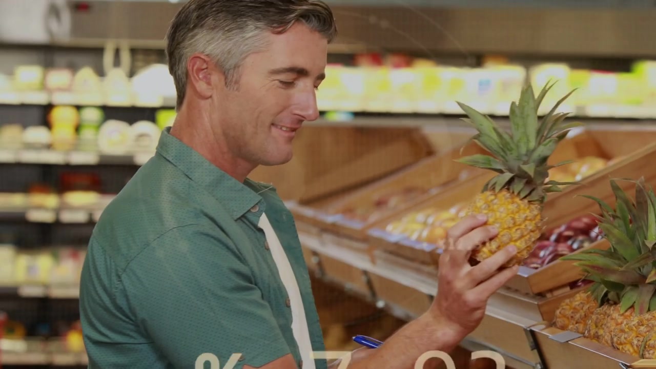 Homme vérifiant des produits frais au détail, tapant sur une tablette et enregistrant des graphiques boursiers superposés aux détails d'un ananas
