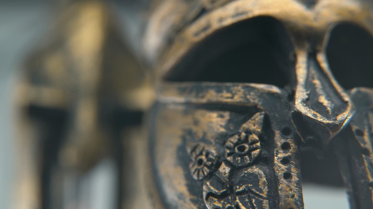 A close-up macro creative shot of a Spartan design, two different ancient warrior metal bronze helmets, glowing textured face mask shapes, studio lighting, 4K cinematic video, Slow Motion, tilt down