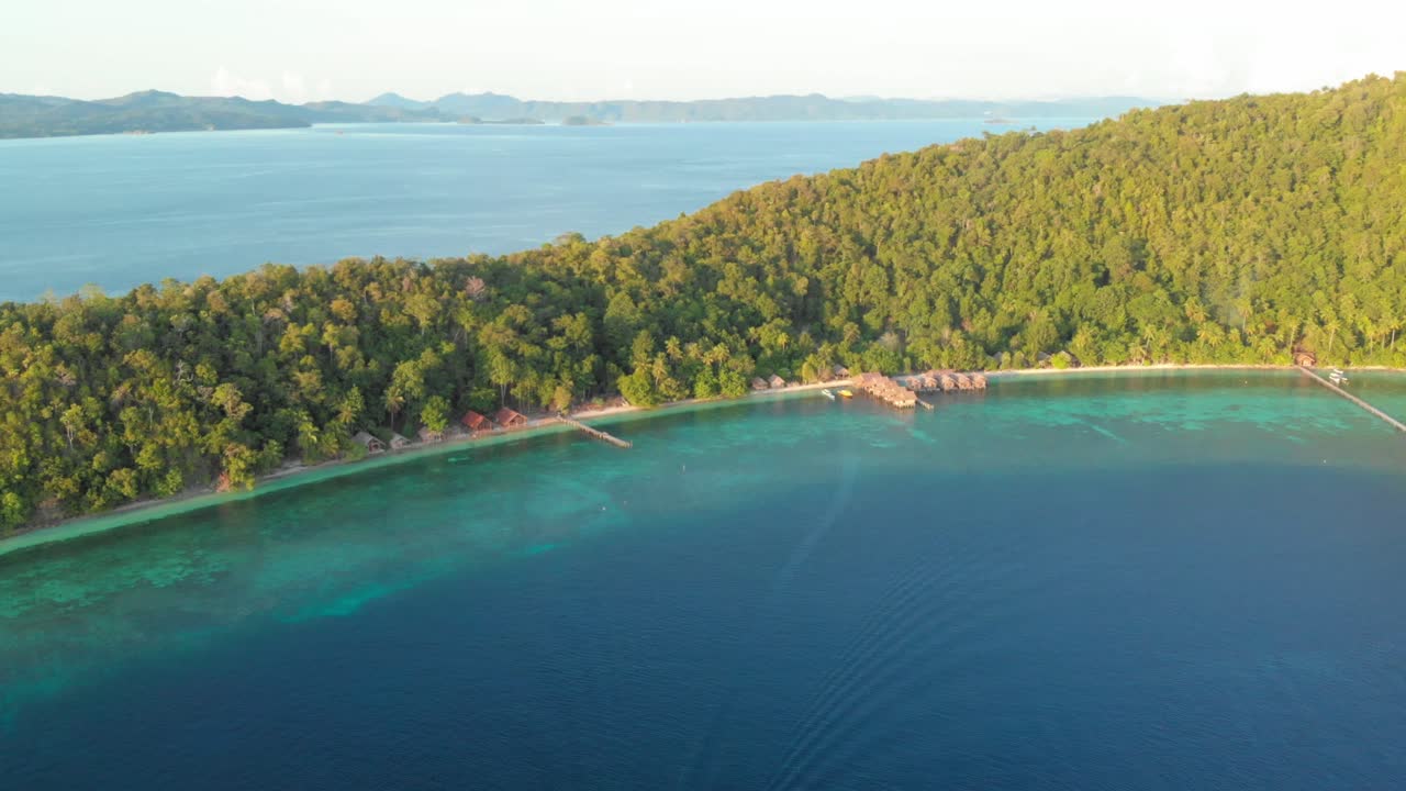 Tropical Island of Kri in Raja Ampat, Indonesia with a boat speeding through the turquoise waters near the shoreline. The shot showcases the entire island, with lush green forest and exotic beach.