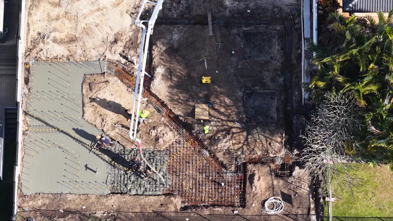 Overhead drone shot of workers pouring concrete foundation over steel reinforcement in Broadbeach Waters, Australia.