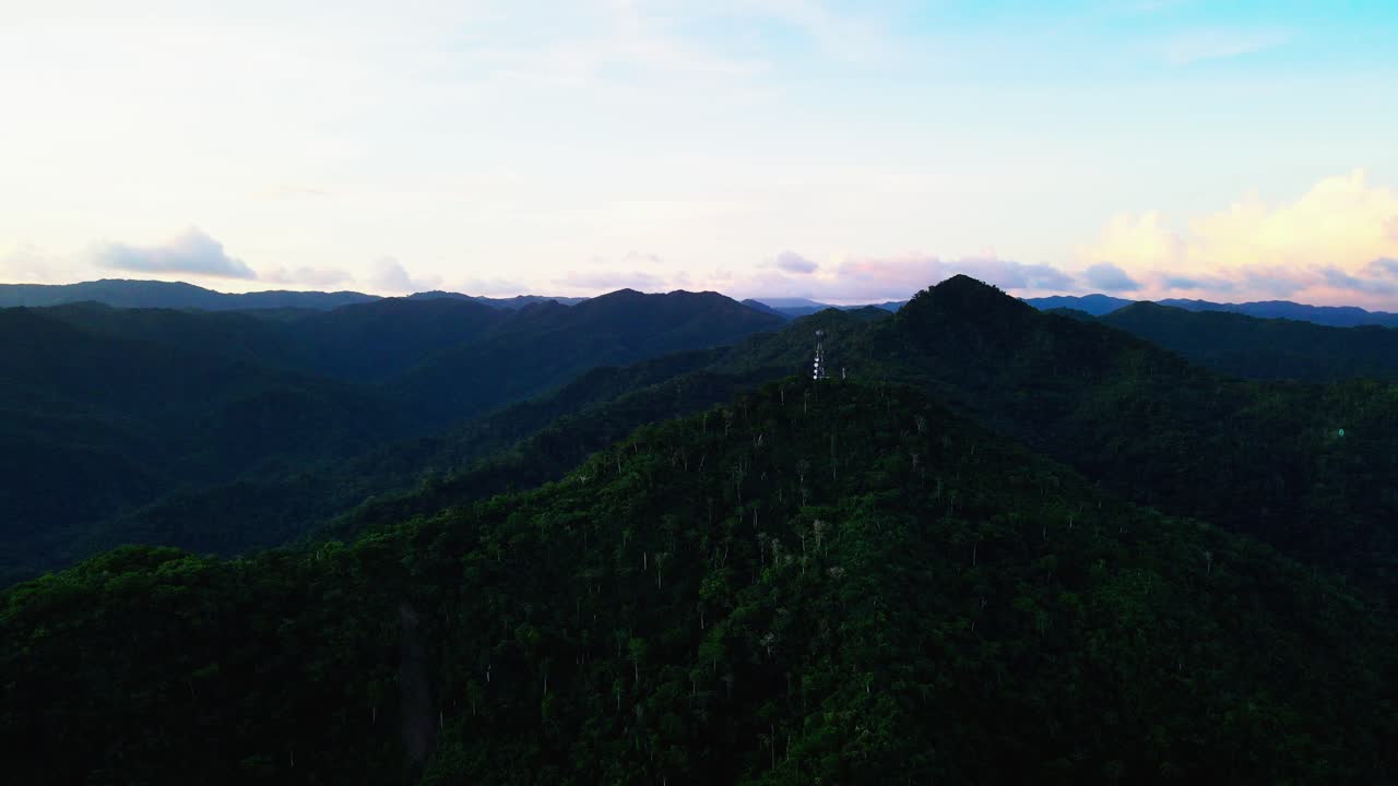 Orbiting aerial view of a mountaintop phone telecommunications tower with lush greenery during sunset at Mount Cagmasuso, Catanduanes, Philippines.